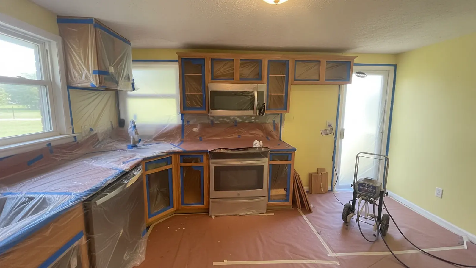 Kitchen cabinets prepared for painting with counters and appliances masked off